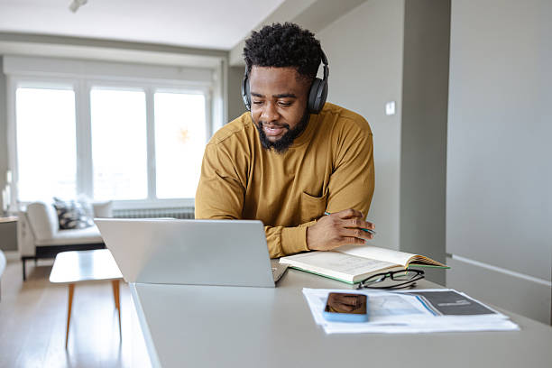Man in headphones working remotely from home using a laptop and taking notes