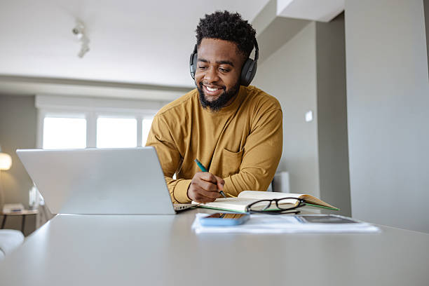 istock Man in headphones working remotely from home using a laptop and taking notes 2209792997