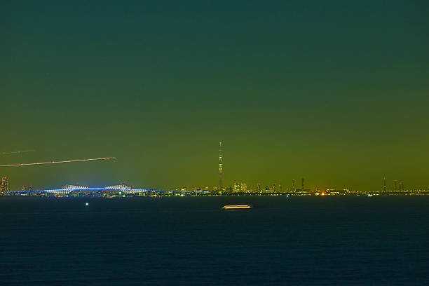 Beyond the vast darkness, along the horizon, the silhouette of an industrial area (petrochemical plant perhaps) twinkles countless artificial lights. The sky above is eerily dyed in an otherworldly green light, like the aurora. Evidence of the intense energy that human activities imprint on the darkness of the night and nature. A sci-fi-like scene unfolds, captivating the viewer, yet somehow stirring up anxiety.