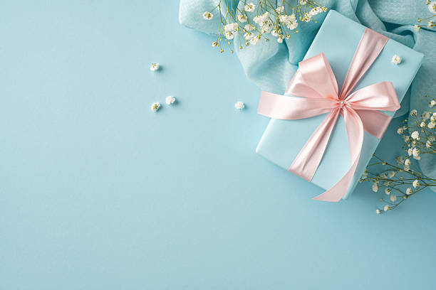 istock Decorative image featuring a delicate gift box adorned with pink ribbon and surrounded by flowers, set on a light blue backdrop to convey celebration, love, and thoughtful appreciation 2209795511