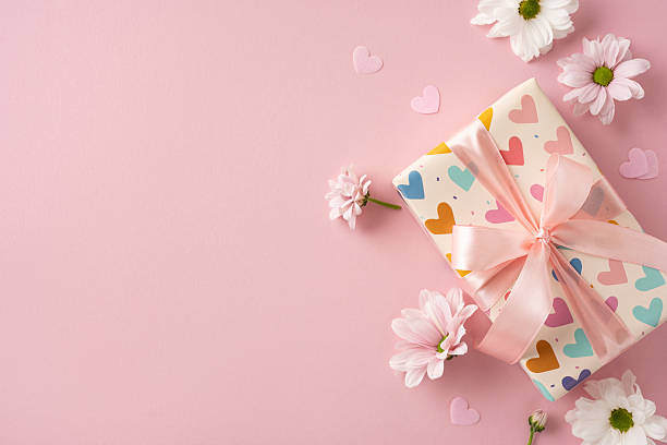 istock Decorative wrapped gift with a soft ribbon placed among flowers on pink background 2209795518
