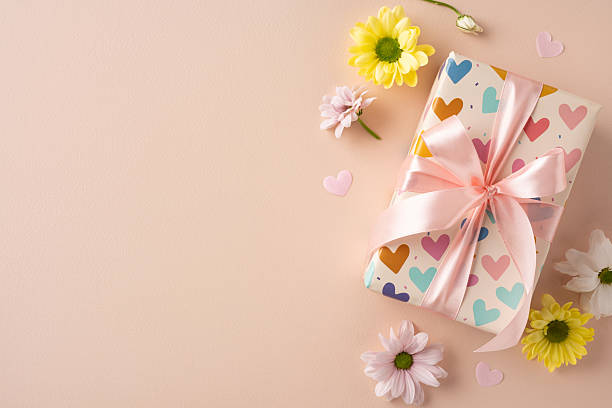 istock Gift box decorated with a bow and colorful hearts surrounded by flowers on a neutral surface 2209795520