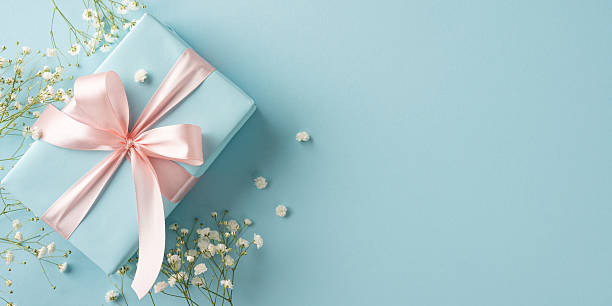 istock Stylish gift box decorated with pink ribbon laying on blue background with tiny flowers 2209795524