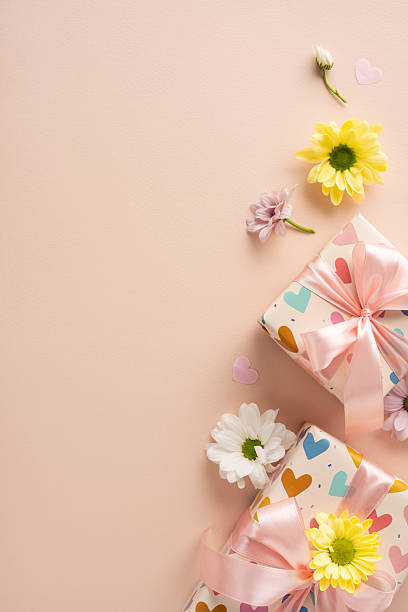 istock Gift boxes wrapped with heart-patterned paper topped with ribbons and daisies placed on a vertical pastel background 2209795530
