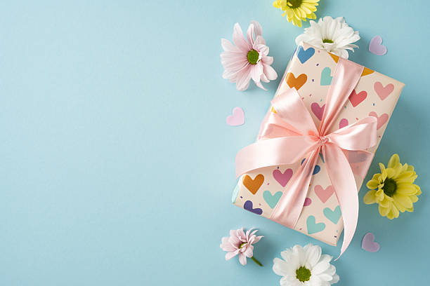 istock Decoratively wrapped gift with a pink ribbon surrounded by daisies on a light blue background 2209795531