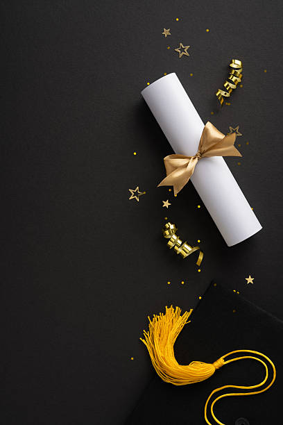 istock Symbolic vertical items for graduation including a diploma scroll tied with gold ribbon on dark surface 2209795533