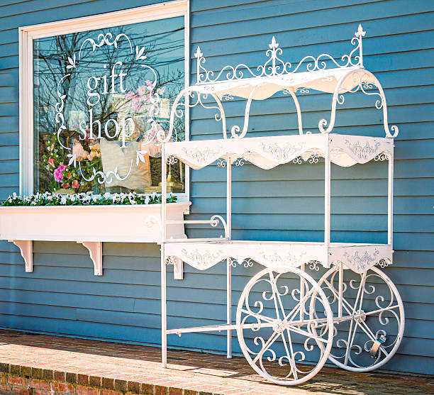 An empty white wrought iron flower cart stands outside a Cape Cod gift shop on an April Morning