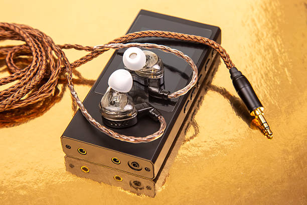 istock Wired earbuds with a woven cable on a sleek black audio player, set on a reflective gold surface. Ideal for technology, sound, and modern design concepts 2209817896