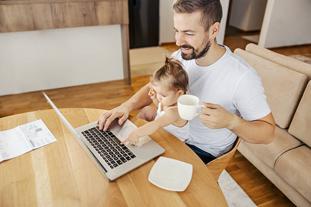 istock A happy remote worker is holding his infant in a lap and working on a laptop while she is helping him. 2209820057