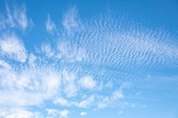 Wispy cirrus clouds and patchy altocumulus formations scatter across the sky, creating a layered texture above a rugged mountain range.