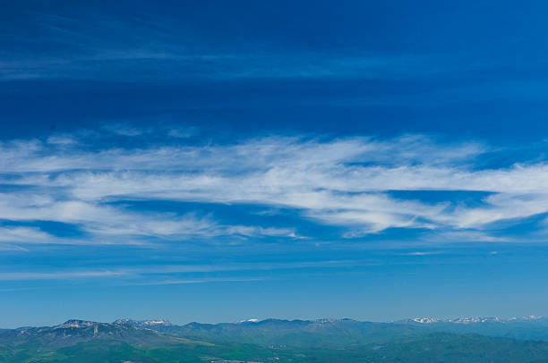 This photo captures the vast blue sky and distant mountains. The sky is a vivid blue with a few thin white clouds. Green mountains line the horizon, creating an open landscape that stretches into the distance.