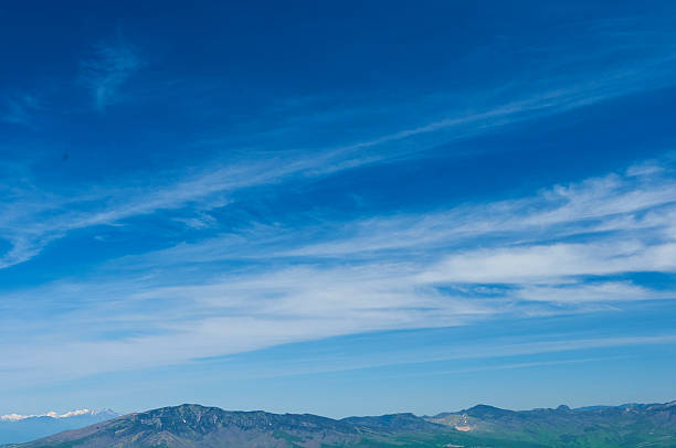 This photo captures the vast blue sky and distant mountains. The sky is a vivid blue with a few thin white clouds. Green mountains line the horizon, creating an open landscape that stretches into the distance.