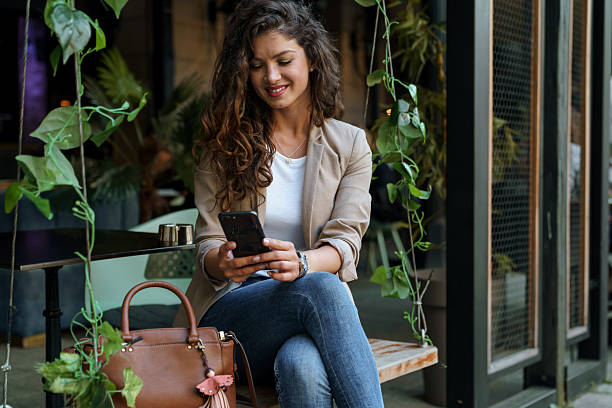 istock Smiling Woman Using Smartphone in Eco-Friendly Coffee Shop with Lush Greenery 2209843011