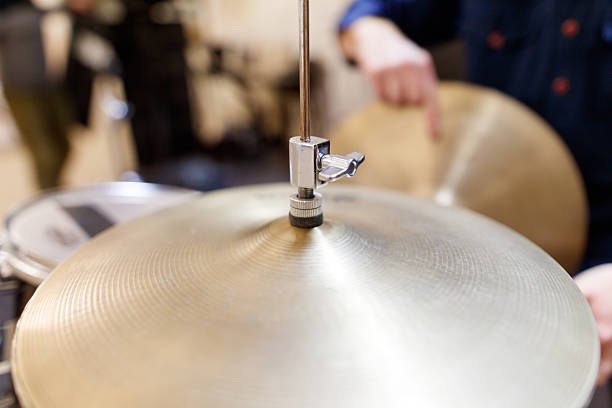 A person is holding a drumstick and pointing at a drum. The drum is a large, golden cymbal