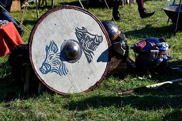 A close up on numerous shields with old Viking crests, sturdy iron helmets, axes, as well as some furs used by medieval warriors, seen during a medieval fair organized in Poland in summer
