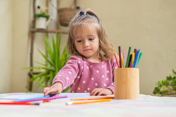 istock Two-year-old girl reaching for colored pencils while sitting at a table, engaging in a creative drawing activity at home, highlighting early childhood development 2209846052