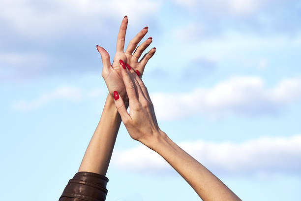 istock Graceful hands with red nails reaching towards blue sky and clouds 2209854402