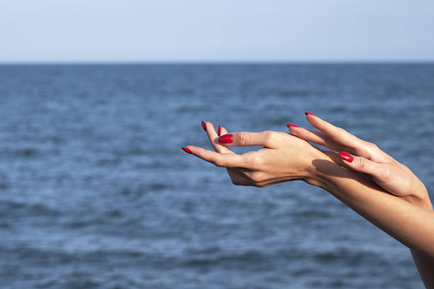 Elegant hands with red nails gesturing above the ocean horizon.