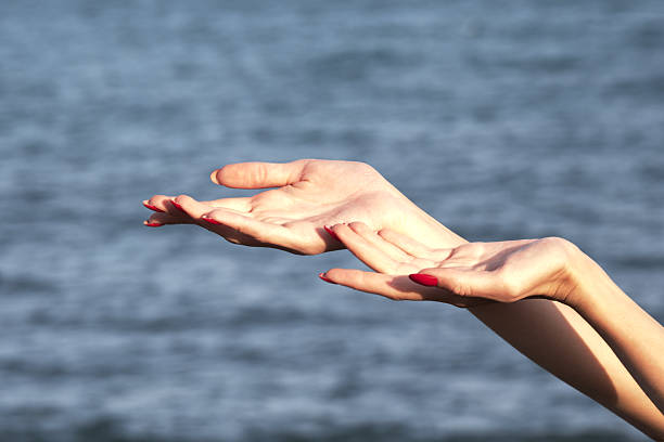 Hands reaching towards blurred waters: elegant gesture with painted nails.