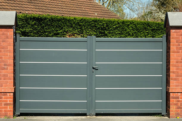 istock A modern grey metal gate with sleek white lines, bordered by red brick pillars, stands closed in front of a lush green hedge. 2209855311