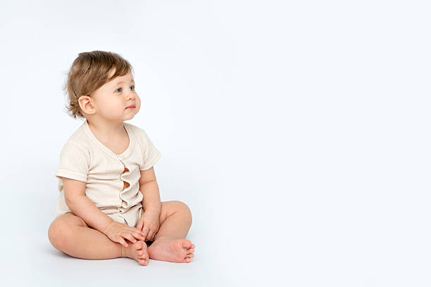 istock A baby boy is sitting on a white isolated background with a place for text in light clothes. A small happy child looks away, space for text. 2209859622