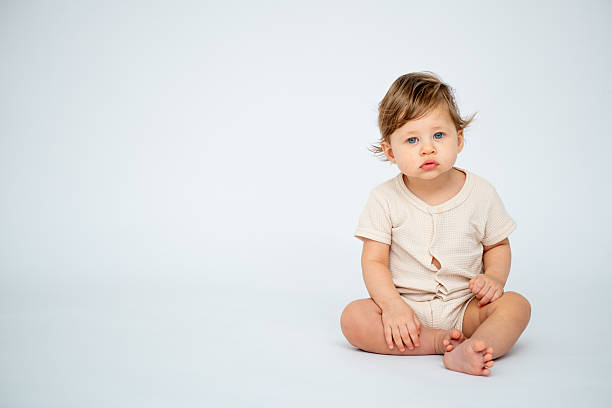 istock A baby boy is sitting on a white isolated background with a place for text in light clothes. A small happy child, space for text 2209859625
