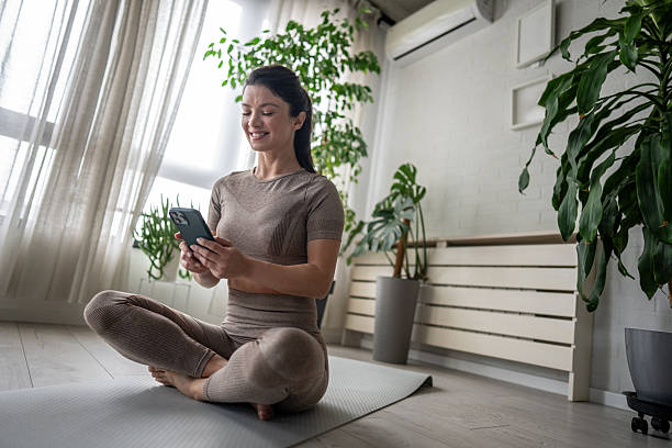 istock Smiling sportswoman using smartphone while sitting on yoga mat at home 2209866794