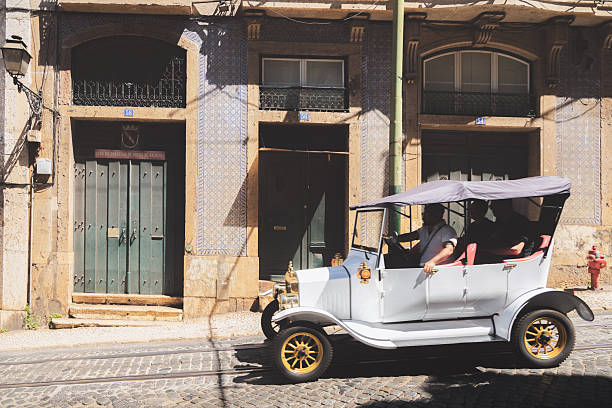 Lisbon, Portugal - July 12 2024: A vintage classic car parked on a cobblestone street in front of a historic building adorned with azulejo tiles, capturing the nostalgic charm of the old town in summer daylight.