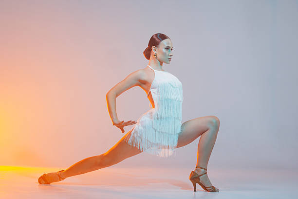 istock Female Latin dancer performs powerful lunge pose in fringe dress under dramatic stage lighting. 2209874971