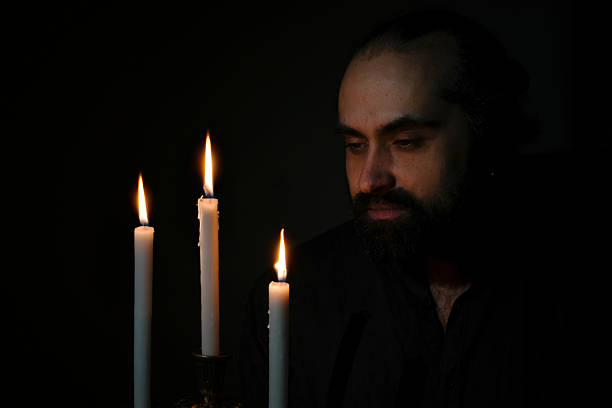 an with a serene expression gazing at candles in a dimly lit room, creating a contemplative and peaceful atmosphere. The scene captures a moment of quiet reflection. High quality photo