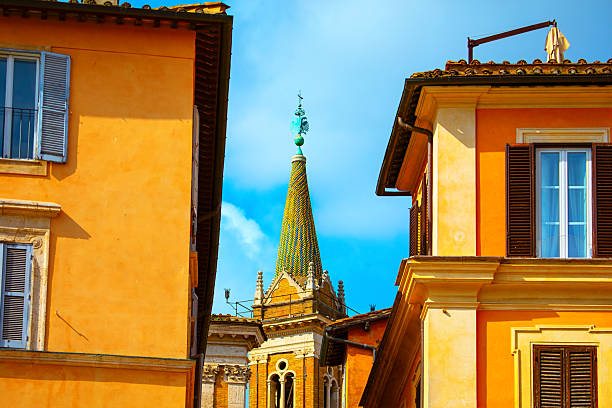 Colorful buildings frame a church spire in Rome, Italy, under a bright sky. Traditional Roman architecture and vivid textures create a warm, inviting cityscape