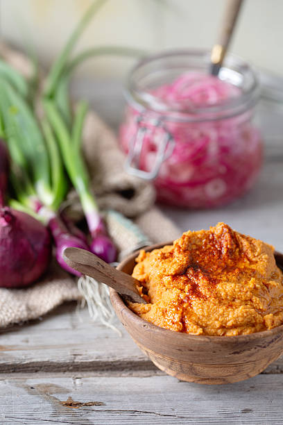 Vibrant orange hummusin a wooden bowl, served with pickled red onions and spring onions. Vegan dip or side dish.