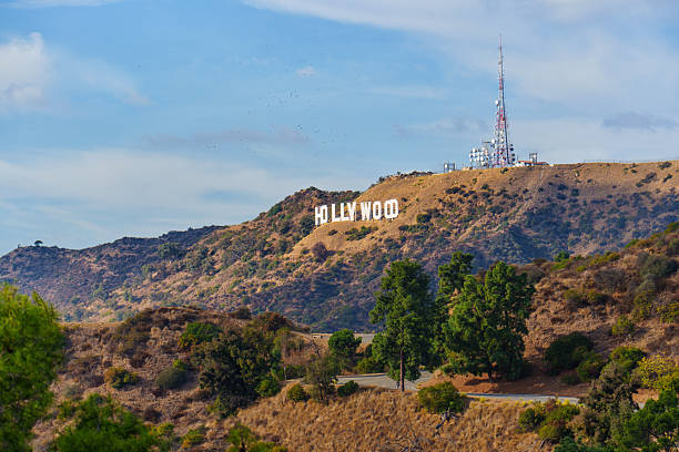Los Angeles, California - December 14, 2024: Iconic Hollywood Sign on the hillside with a nearby broadcast tower, surrounded by lush greenery and a clear blue sky.