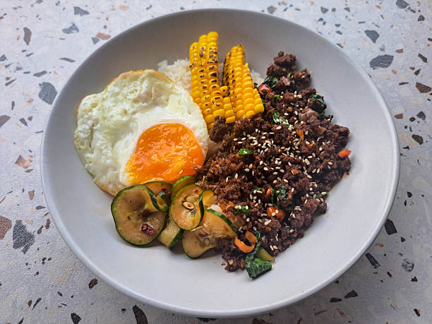 istock Serving Of Beef Holy Basil With Steam Rice, Minced Beef, Sunny Side Up, Grilled Corn, Pickled Cucumber And Basil Leaf. Food Menu. 2209895810