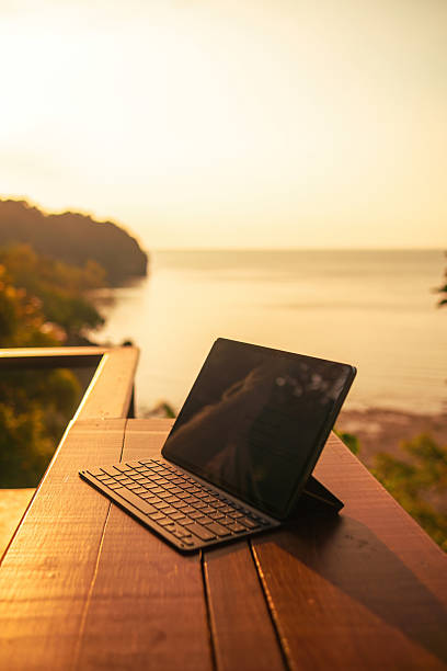 istock Tablet with keyboard on wood table overlooking ocean at sunset 2209896075