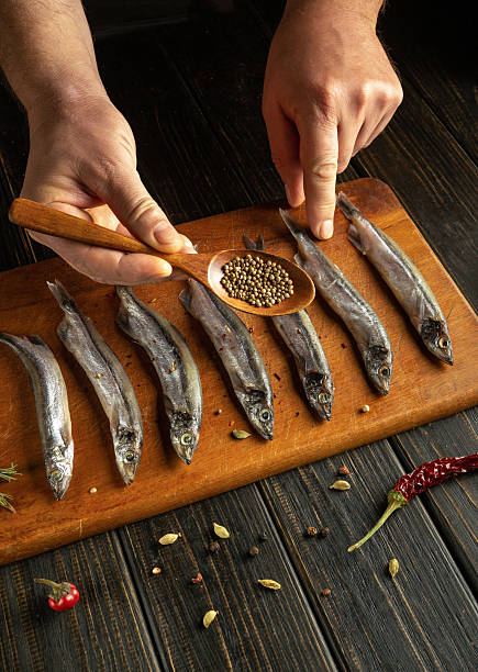 istock Hands carefully arrange fresh fish on a wooden board, adding spices from a small spoon, creating a flavorful dish in a cozy kitchen setting 2209900322