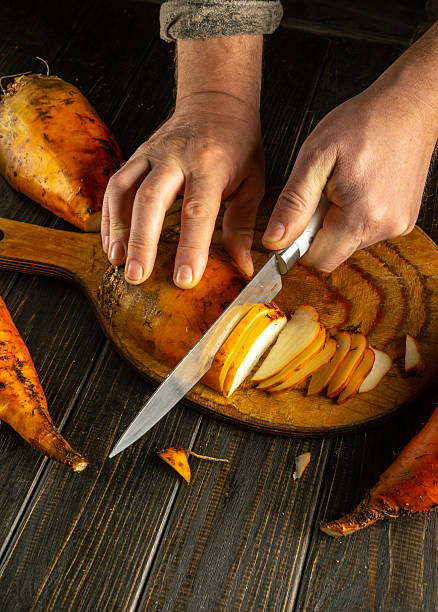 istock Hands skillfully slice sweet potatoes on a wooden cutting board, surrounded by fresh vegetables in a warm, inviting kitchen. The process highlights the joy of cooking 2209900439