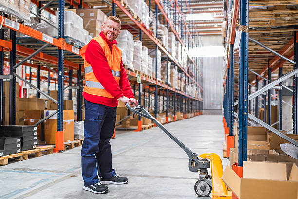 istock Warehouse worker moving boxes with pallet jack in logistics center 2209922225