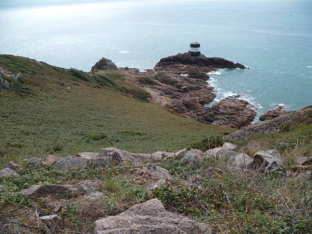 A small lighthouse black and white seen from the coast of Jersey on a sunny day
