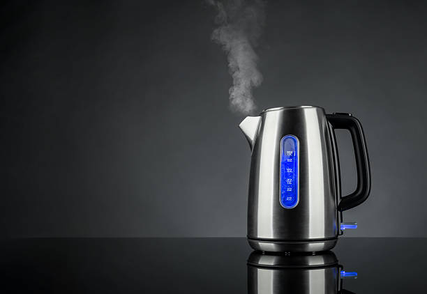 istock Electric kettle boiling water with steam rising, placed on a glossy black surface. Stainless steel body with blue illuminated water level indicator on dark gradient background. 2209922300