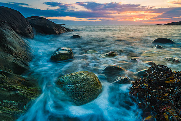 Coastal scenery at sunset in Sweden showcasing waves lapping against rocks and reflecting warm hues in the sky