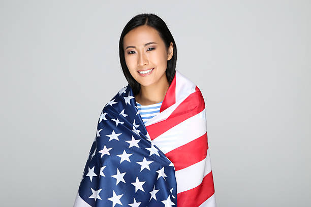 istock Young woman wrapped in American flag on grey background 2209930788