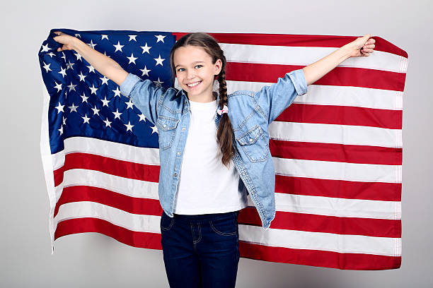 istock Young girl holding an American flag on grey background 2209936323