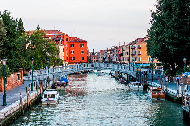 Venice, Italy. August 10th, 2010: A charming view of a Venetian canal, with a bridge crossing over the water. The colorful buildings lining the canal create a vibrant contrast against the calm water, capturing the essence of Venice's unique architectural beauty.