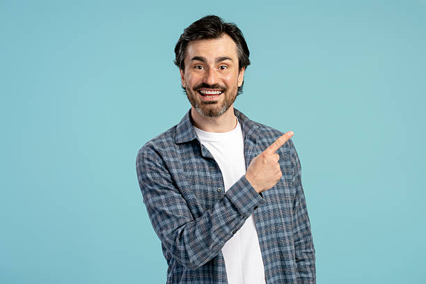 istock Smiling man pointing finger showing something on blue background 2209937593