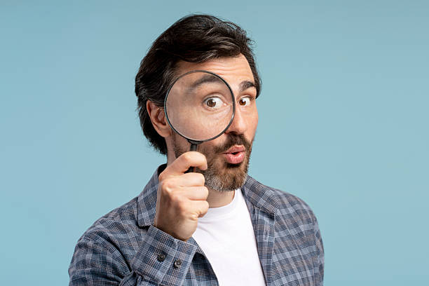istock Curious man holding magnifying glass making funny face 2209937598