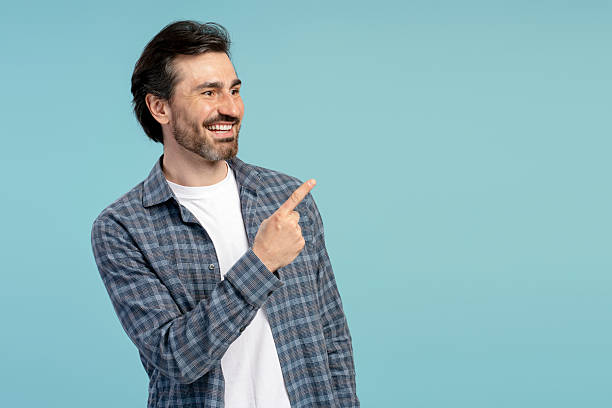 istock Smiling man pointing finger showing something on blue background 2209937599
