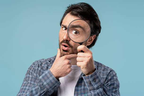istock Curious man examining something with magnifying glass on blue background 2209937603