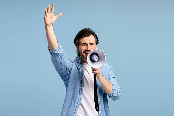 istock Activist raising hand while speaking into megaphone on blue background 2209937648