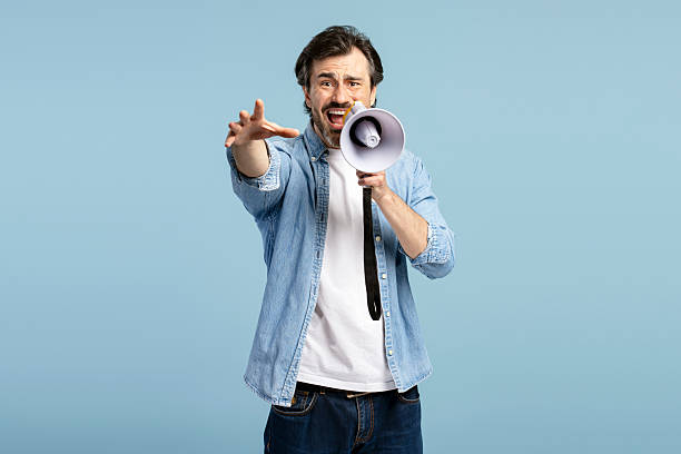 istock Serious man shouting through megaphone and pointing finger on blue background 2209937669